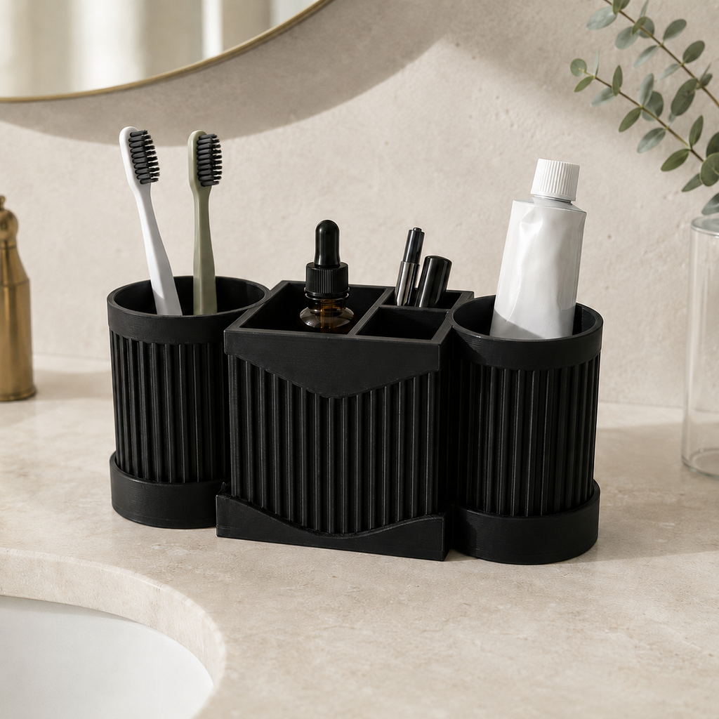 A black three-compartment toothbrush holder set on a bathroom counter, holding two toothbrushes, a dropper bottle, pens, and a tube of toothpaste.