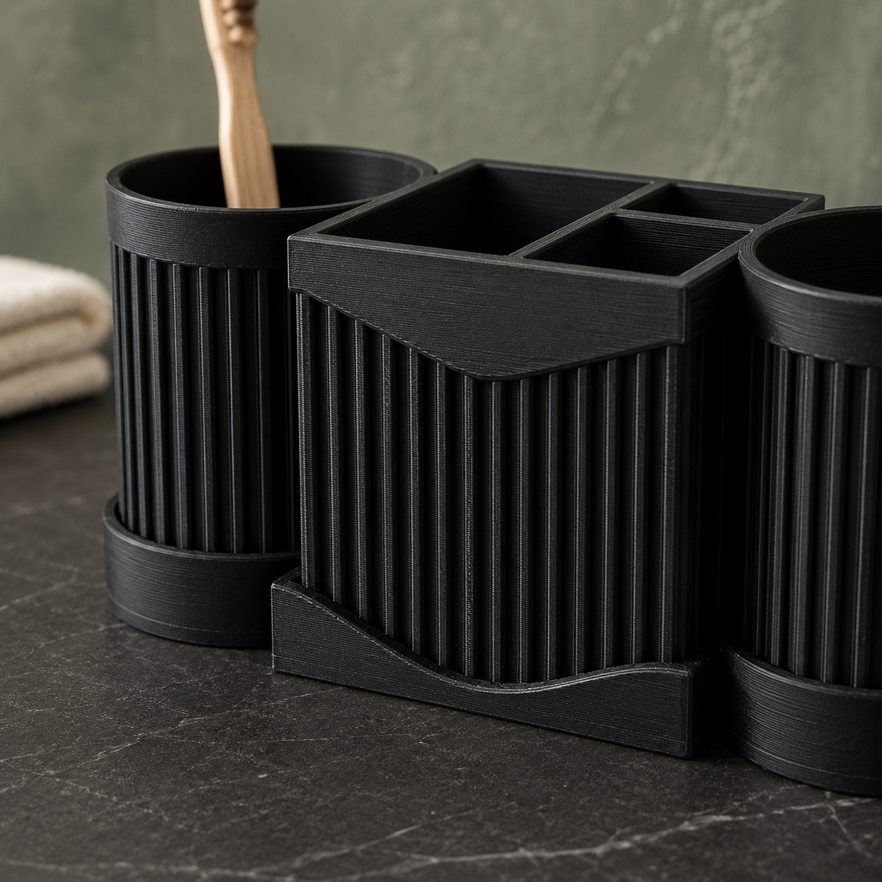 Three-piece black ribbed bathroom organizer set including two toothbrush holders and one multi-compartment tray, arranged on a dark marble countertop with a folded towel and green wall in the background.