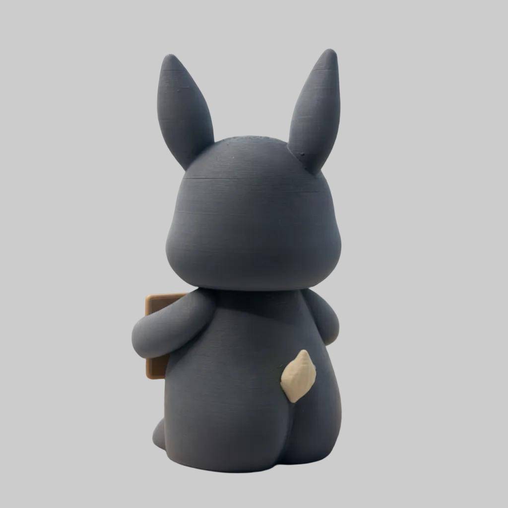 Gray plush toy with rabbit-like features sitting on a path in a natural landscape.