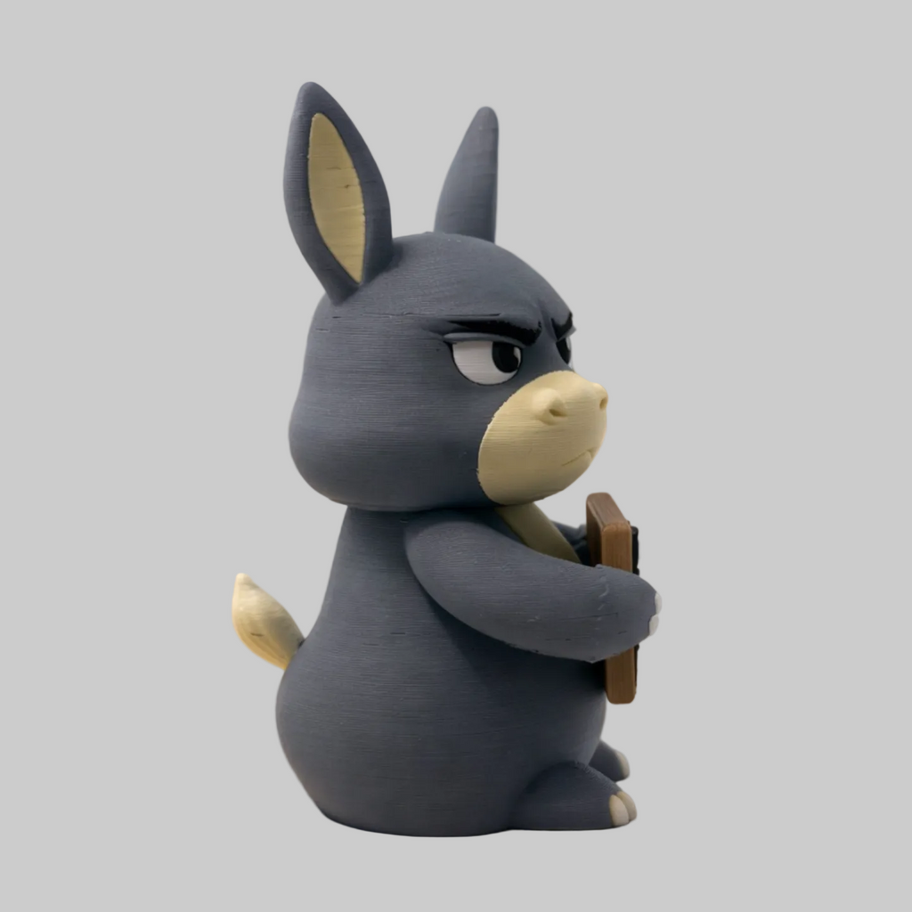 A stylized 3D-rendered gray donkey-like character with a beige snout and ears sits on a dirt path in a rocky outdoor landscape, holding a brown rectangular object.